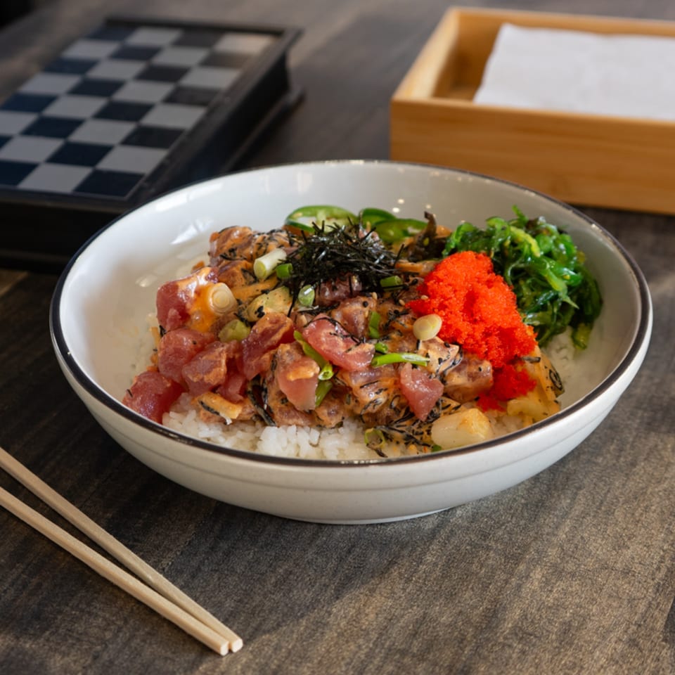 Hana Poke bowl with tuna, tobiko, seaweed, and jalapeños, with chopsticks and a chessboard.